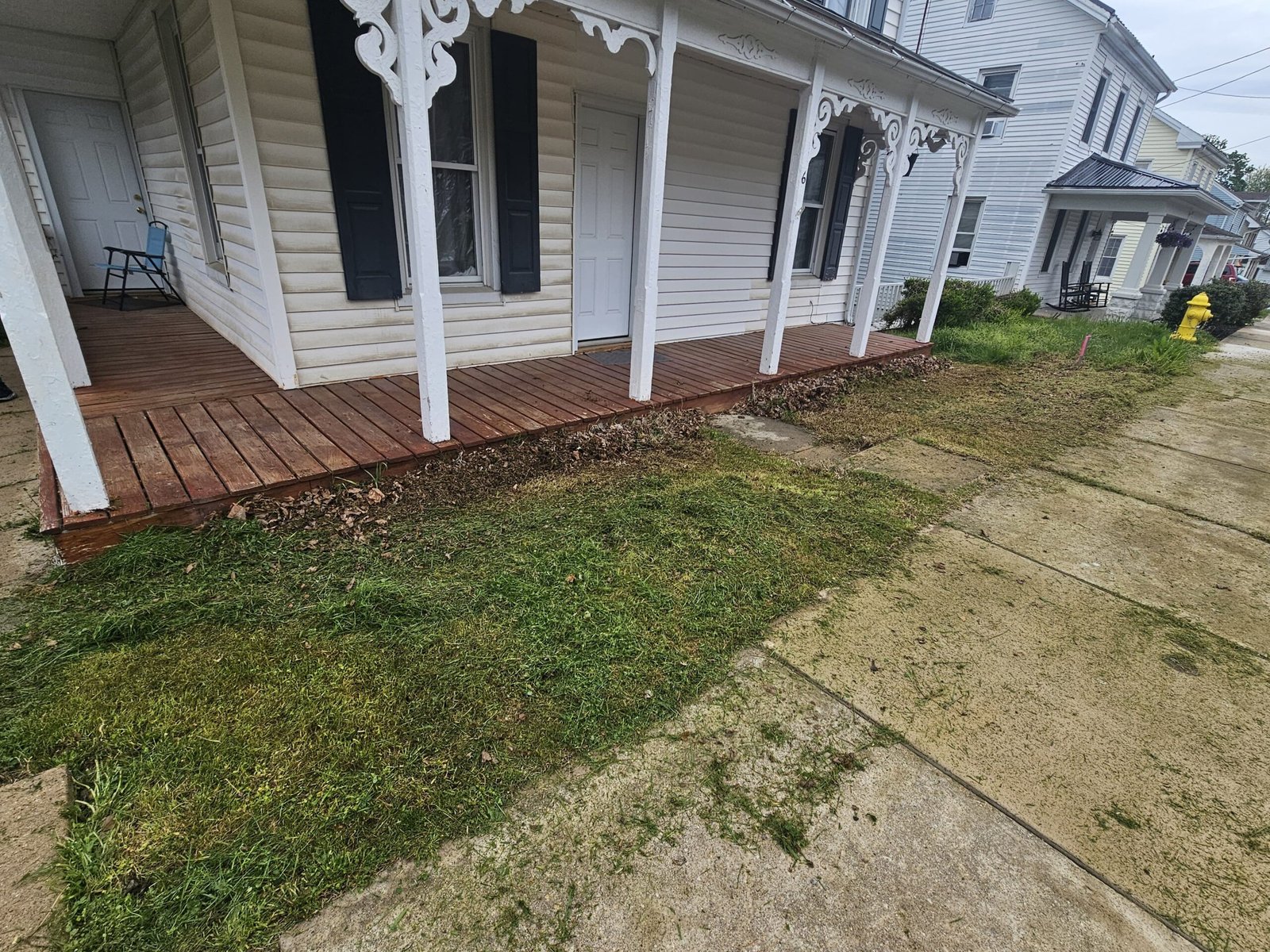 Freshly cut grass along a sidewalk in front of a porch with clippings visible on the concrete
