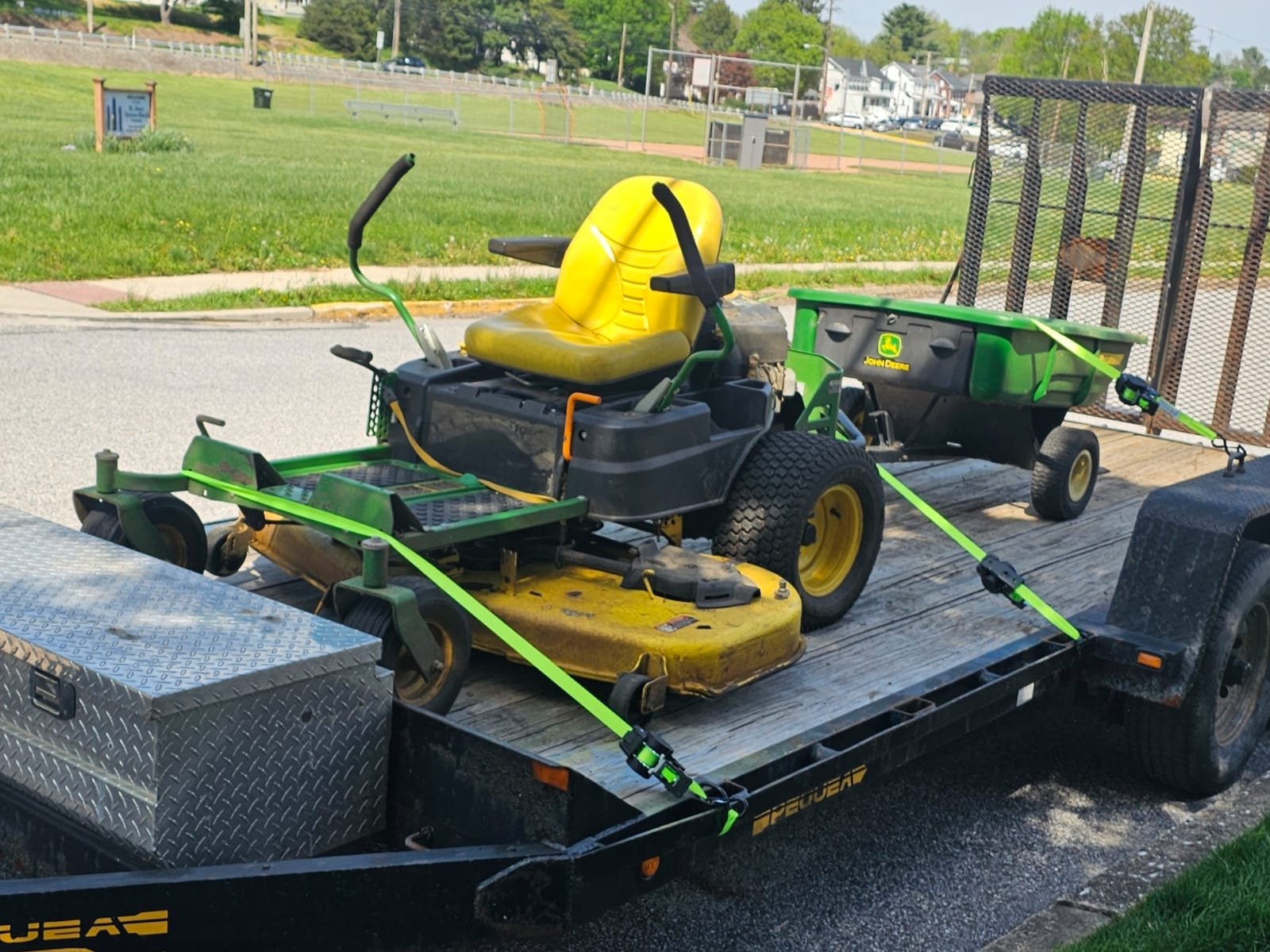 Riding lawn mower secured with straps on a utility trailer parked near a grassy area
